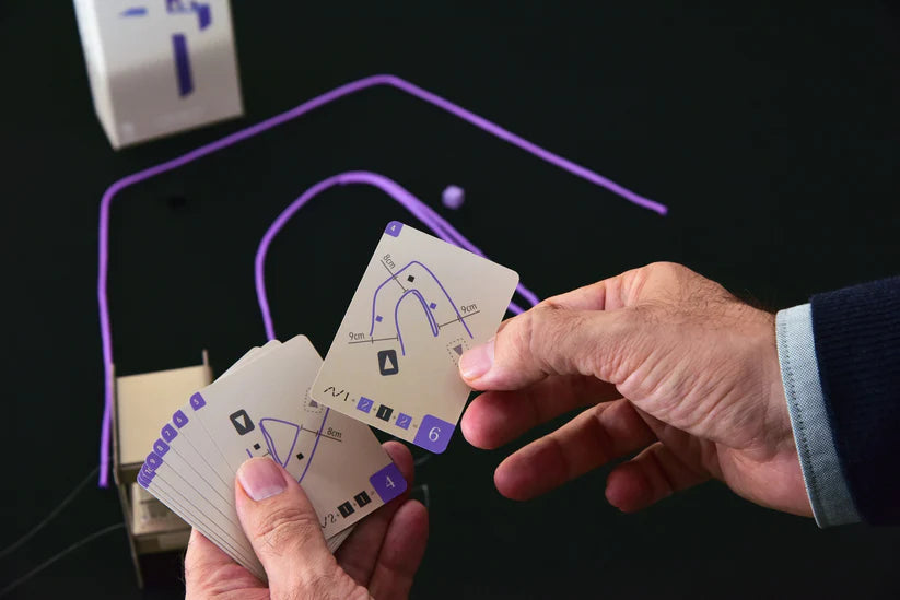 Manos sosteniendo tarjetas con emblemas, junto a cajas y cable morado